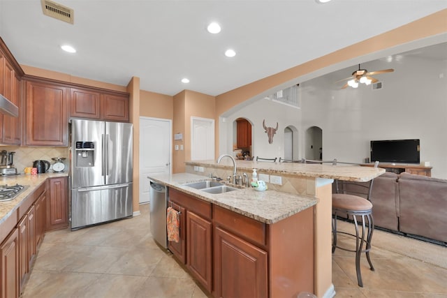 kitchen with appliances with stainless steel finishes, a breakfast bar, sink, decorative backsplash, and a kitchen island with sink