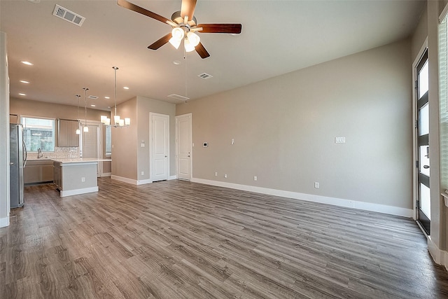 unfurnished living room with hardwood / wood-style flooring, ceiling fan with notable chandelier, and sink