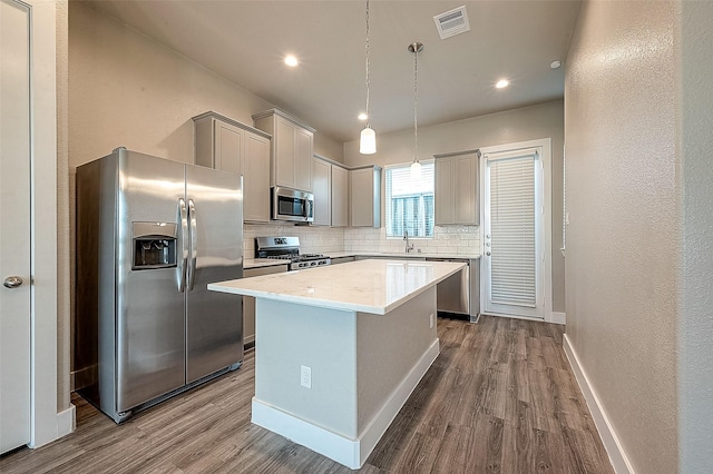 kitchen with appliances with stainless steel finishes, pendant lighting, sink, decorative backsplash, and a center island