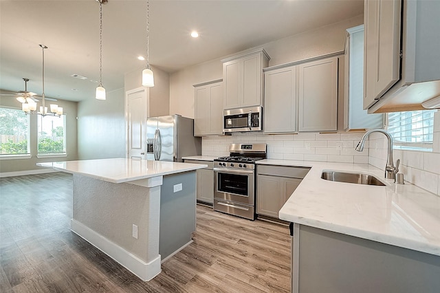 kitchen featuring gray cabinets, a kitchen island, sink, hanging light fixtures, and stainless steel appliances