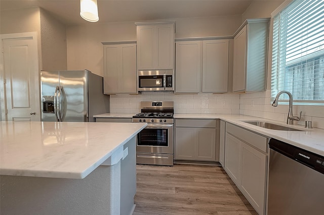 kitchen with sink, stainless steel appliances, light stone countertops, decorative backsplash, and light wood-type flooring