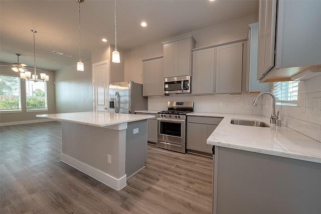 kitchen with pendant lighting, sink, appliances with stainless steel finishes, light stone countertops, and a kitchen island