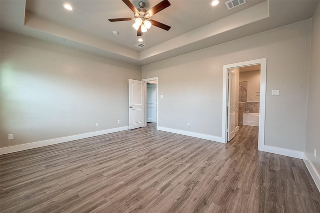 unfurnished bedroom featuring a raised ceiling, ensuite bathroom, hardwood / wood-style flooring, and ceiling fan