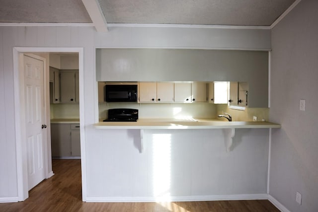 kitchen with beamed ceiling, dark hardwood / wood-style floors, kitchen peninsula, and black appliances