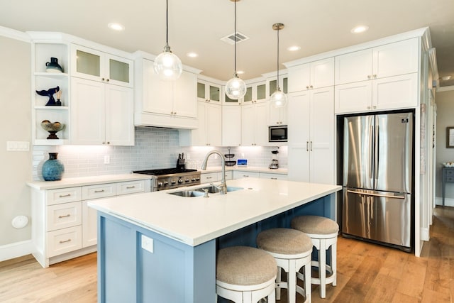 kitchen with sink, appliances with stainless steel finishes, a kitchen island with sink, white cabinets, and decorative light fixtures