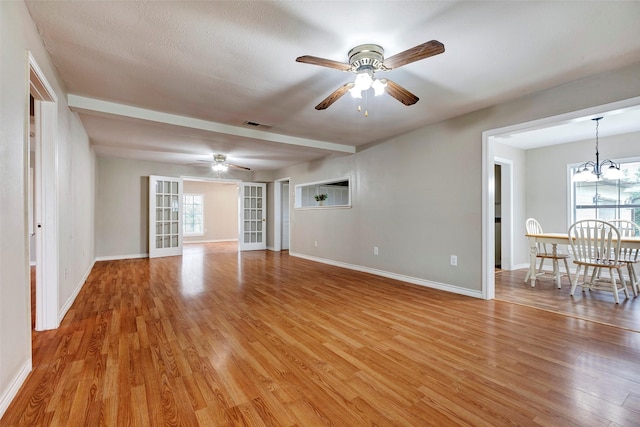 unfurnished living room with ceiling fan with notable chandelier and light hardwood / wood-style flooring