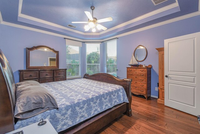 bedroom with crown molding, dark hardwood / wood-style floors, ceiling fan, and a tray ceiling