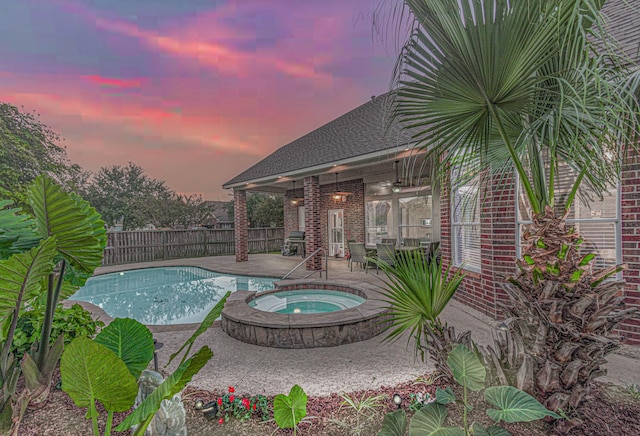 pool at dusk featuring an in ground hot tub, ceiling fan, and a patio