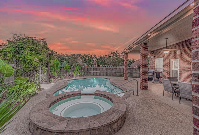 pool at dusk featuring an in ground hot tub, grilling area, and a patio area