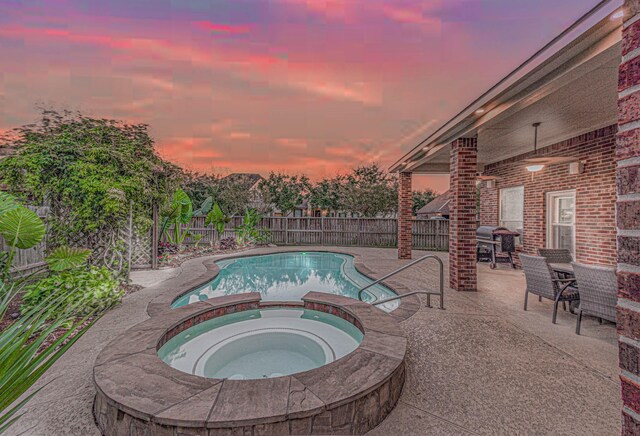 pool at dusk with an in ground hot tub, a grill, and a patio