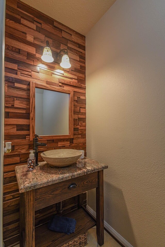 bathroom featuring vanity, wooden walls, and a textured ceiling