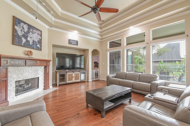 living room featuring crown molding, ceiling fan, hardwood / wood-style floors, a stone fireplace, and a raised ceiling