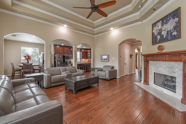 living room with dark wood-type flooring, ornamental molding, a fireplace, and a raised ceiling