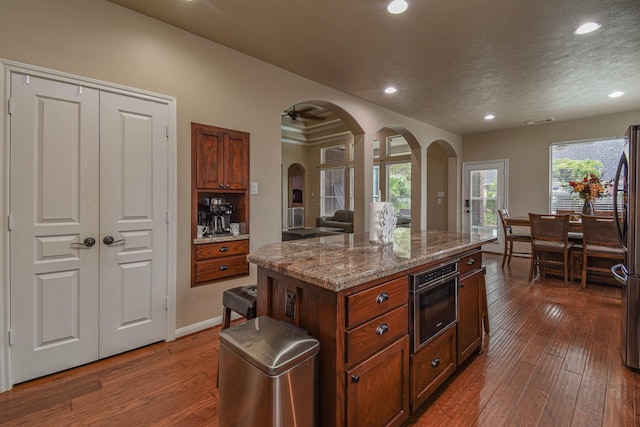 kitchen with a kitchen island, stone countertops, a textured ceiling, and dark hardwood / wood-style floors