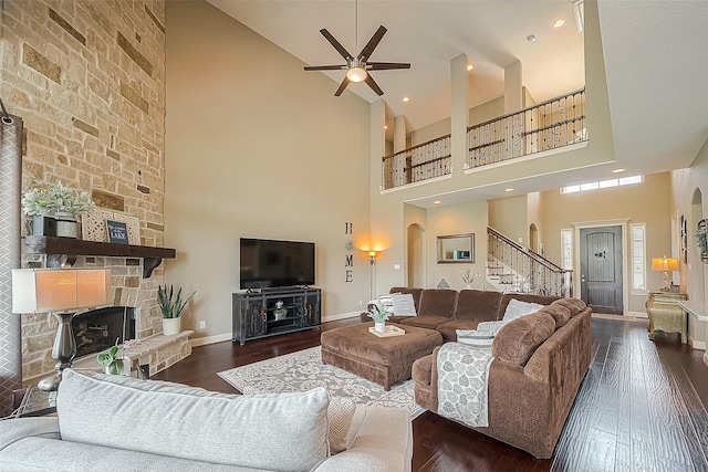 living room with dark wood-type flooring, a fireplace, ceiling fan, and a high ceiling