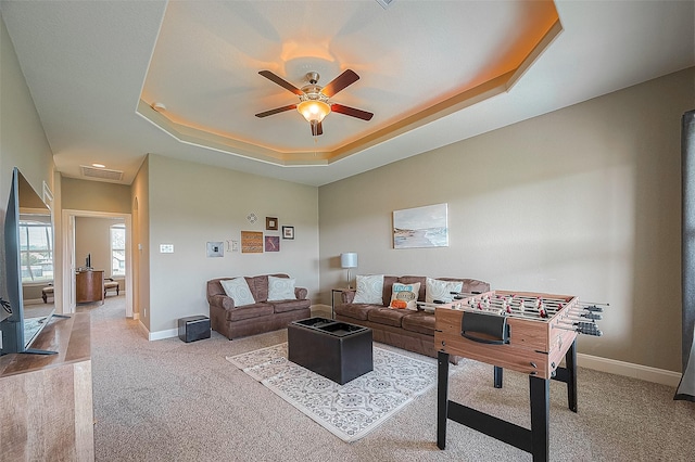 living room with ceiling fan, a raised ceiling, and light carpet