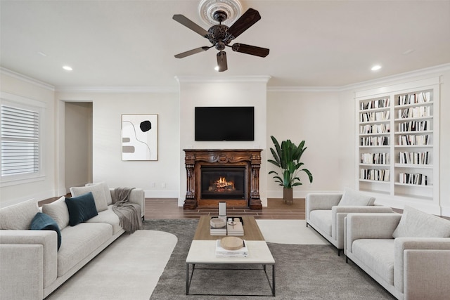 living area with ornamental molding, a glass covered fireplace, wood finished floors, and ceiling fan