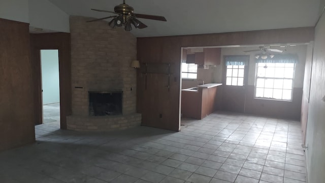 unfurnished living room featuring ceiling fan, vaulted ceiling, a brick fireplace, and light tile patterned floors