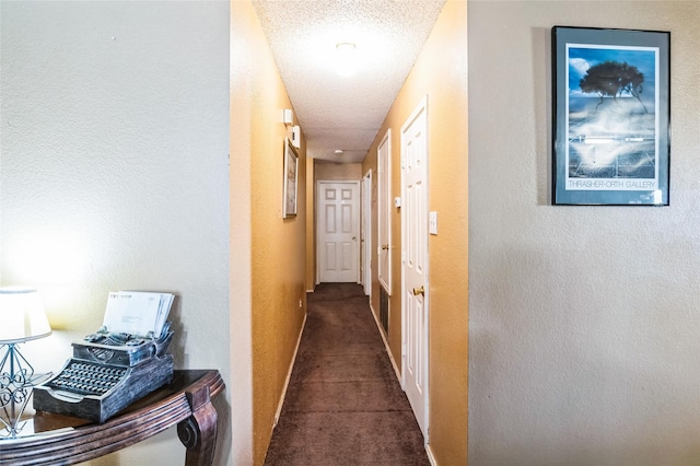 corridor featuring a textured ceiling and dark colored carpet