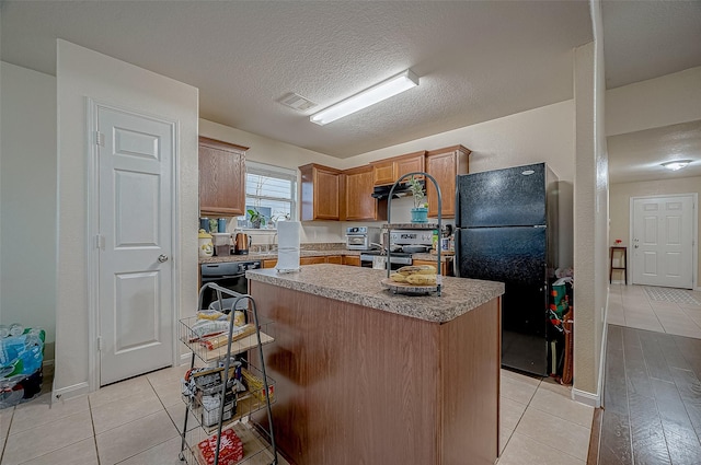 kitchen with dishwasher, black refrigerator, stainless steel range with electric stovetop, a center island, and a kitchen bar