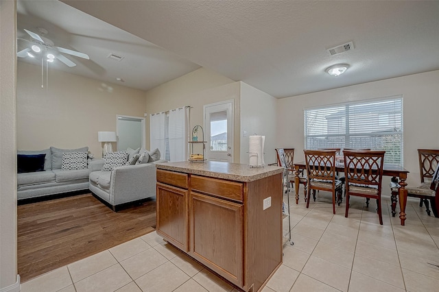 kitchen featuring light tile patterned flooring, ceiling fan, a center island with sink, and a textured ceiling