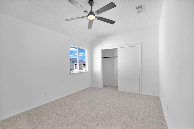 unfurnished bedroom with lofted ceiling, a textured ceiling, carpet floors, a closet, and ceiling fan