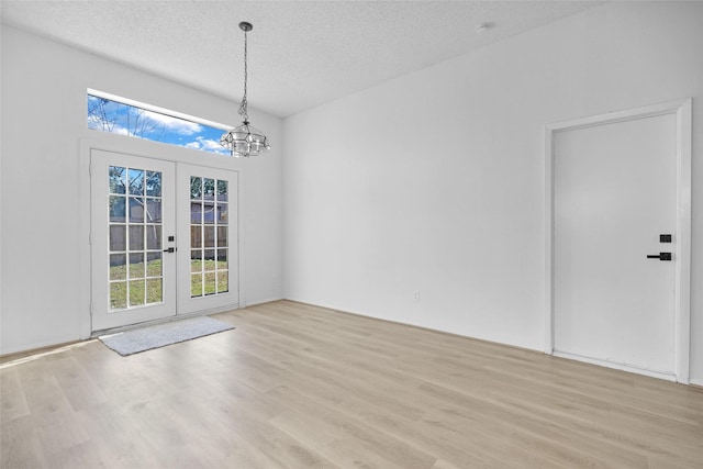 unfurnished dining area featuring a notable chandelier, light hardwood / wood-style floors, french doors, and a textured ceiling