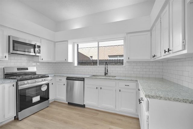 kitchen with sink, tasteful backsplash, light wood-type flooring, stainless steel appliances, and white cabinets