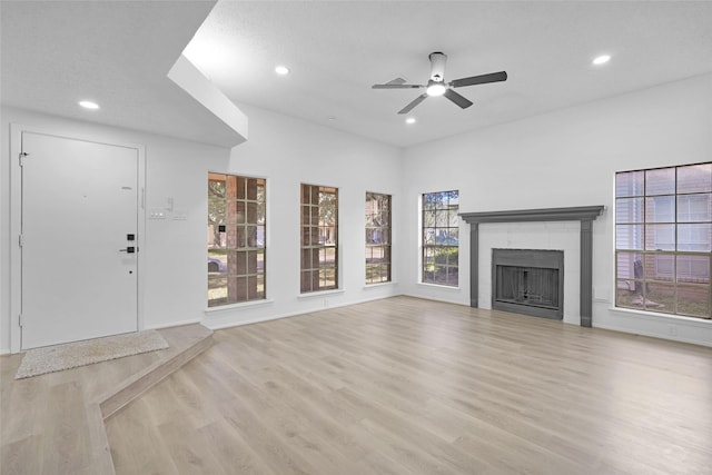 unfurnished living room with ceiling fan, a tiled fireplace, and light wood-type flooring