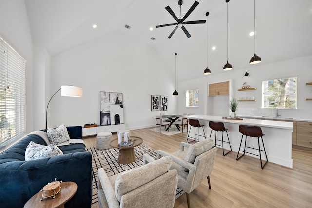 living room featuring sink, light hardwood / wood-style flooring, high vaulted ceiling, and ceiling fan