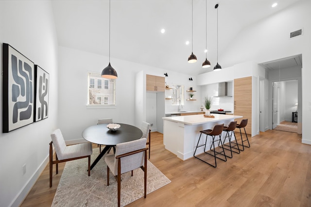 kitchen with hanging light fixtures, a kitchen breakfast bar, a center island, light hardwood / wood-style floors, and wall chimney exhaust hood