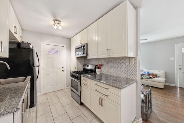 kitchen with sink, dark stone countertops, appliances with stainless steel finishes, white cabinets, and backsplash