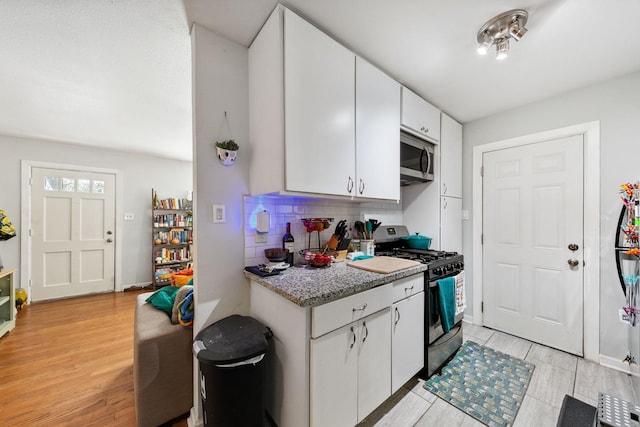 kitchen with stainless steel appliances, white cabinetry, backsplash, and light wood-type flooring