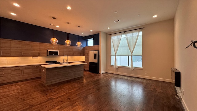 kitchen with sink, hanging light fixtures, a center island with sink, dark hardwood / wood-style floors, and paneled fridge