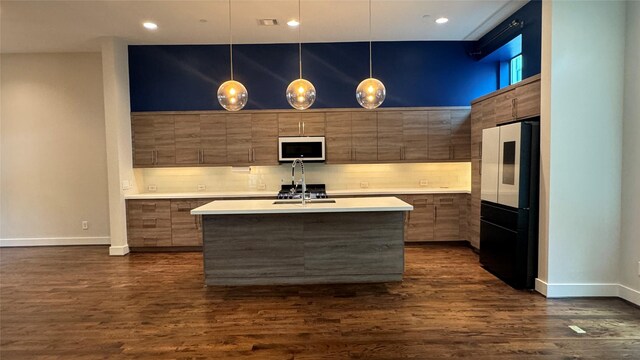 kitchen featuring dark hardwood / wood-style floors, a kitchen island with sink, pendant lighting, and refrigerator