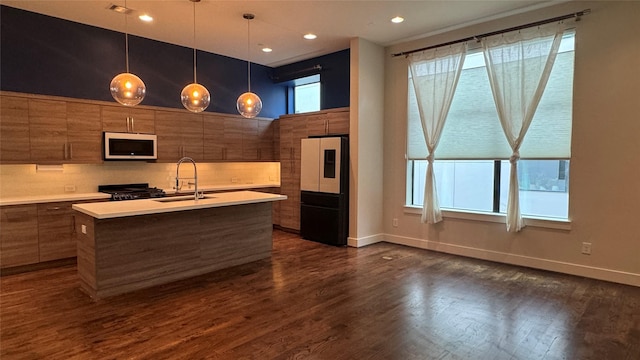 kitchen with sink, a center island with sink, dark hardwood / wood-style floors, pendant lighting, and stove