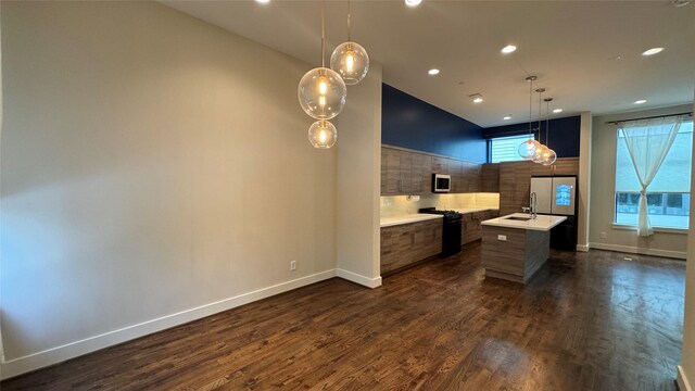 kitchen with dark wood-type flooring, a kitchen island with sink, hanging light fixtures, stainless steel appliances, and decorative backsplash