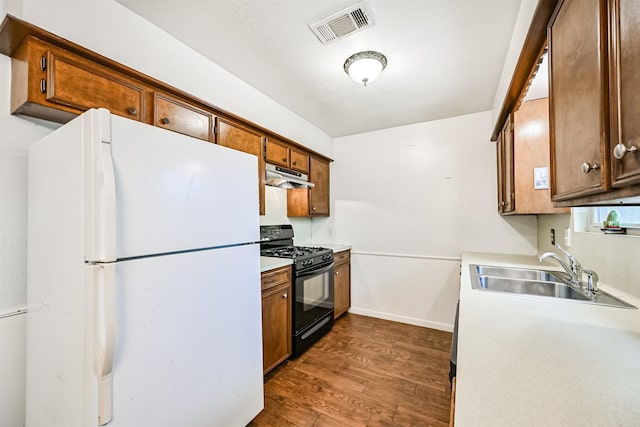 kitchen with dark wood-type flooring, black range with gas stovetop, sink, and white fridge