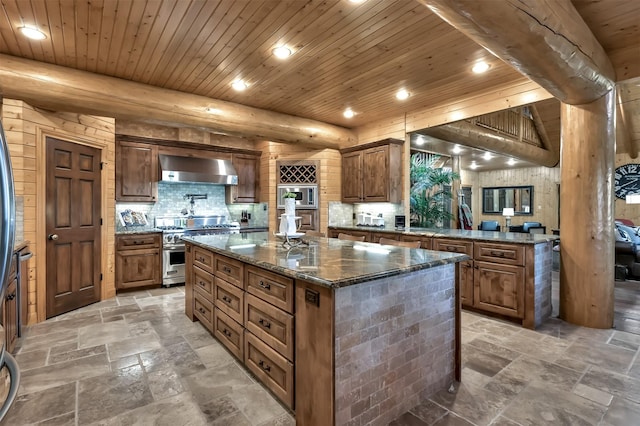 kitchen with wall chimney range hood, wood ceiling, appliances with stainless steel finishes, dark stone countertops, and a center island