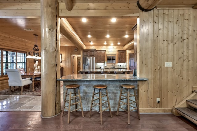 kitchen with dark stone countertops, a breakfast bar area, stainless steel fridge, and wood ceiling