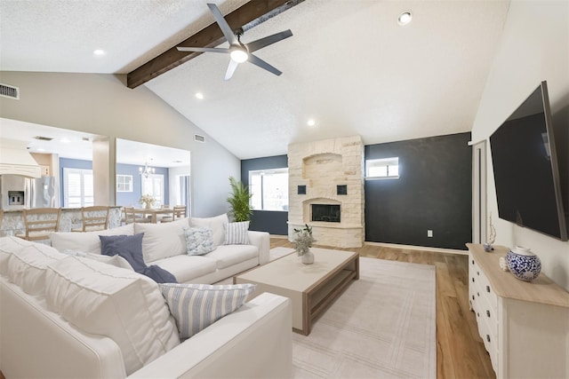 living room with lofted ceiling with beams, a textured ceiling, light wood-type flooring, a fireplace, and ceiling fan with notable chandelier