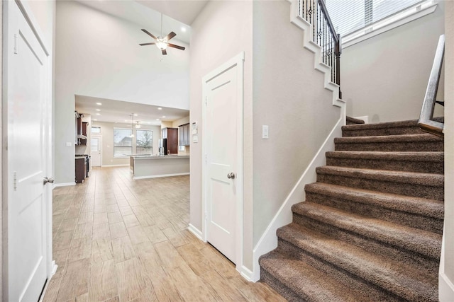 stairway with wood-type flooring, a towering ceiling, and ceiling fan