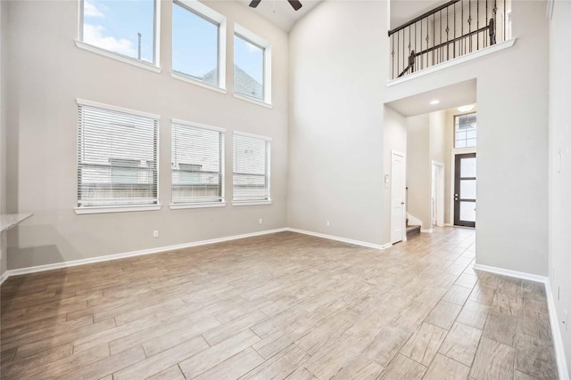 unfurnished living room featuring a towering ceiling, light hardwood / wood-style flooring, and ceiling fan