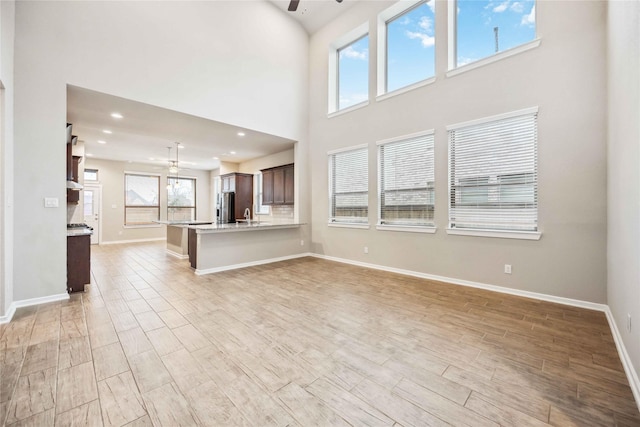 unfurnished living room with ceiling fan, sink, light hardwood / wood-style floors, and a high ceiling