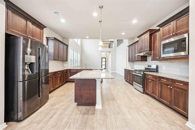 kitchen featuring a kitchen island, appliances with stainless steel finishes, a breakfast bar, pendant lighting, and light stone countertops