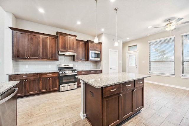 kitchen featuring stainless steel appliances, a center island, light stone counters, decorative backsplash, and decorative light fixtures