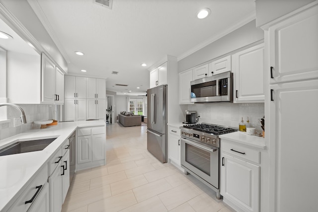 kitchen with sink, white cabinets, decorative backsplash, ornamental molding, and stainless steel appliances