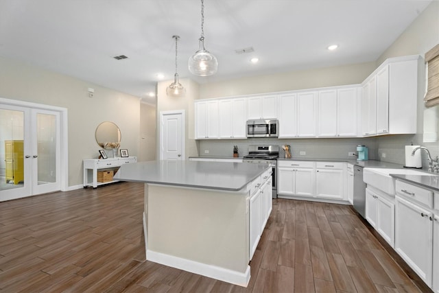 kitchen with backsplash, stainless steel appliances, white cabinets, a kitchen island, and decorative light fixtures