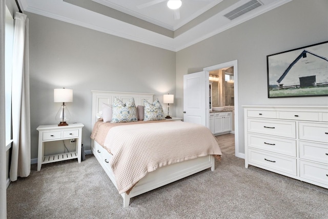 bedroom featuring light colored carpet, ornamental molding, a tray ceiling, and ensuite bath