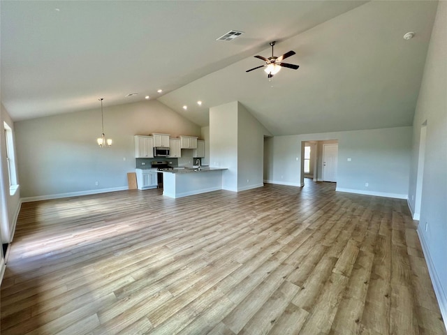 unfurnished living room with high vaulted ceiling, ceiling fan with notable chandelier, and light hardwood / wood-style floors